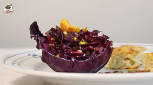 Rotkohlsalat ist in einem Rotkohlblatt angerichtet. Darauf liegt ein Cashewkern.