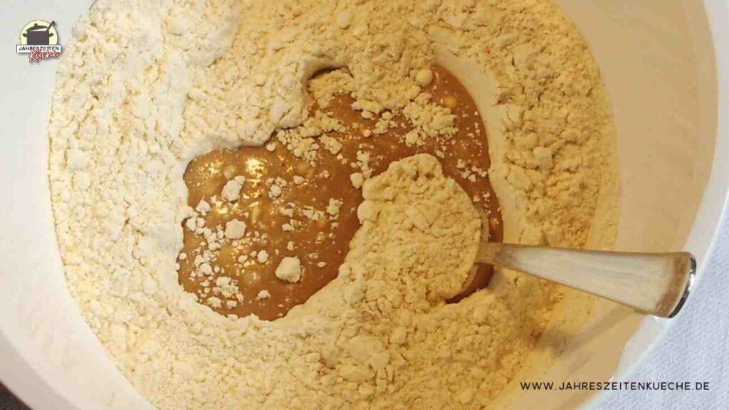 In einer weißen Schüssel steckt ein Löffel, um Mehl mit dem Vorteig zu verrühren