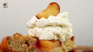 Auf einem Stück Apfel-Pflaumen-Kuchen mit Schlagsahne liegt eine Pflaumensscheibe