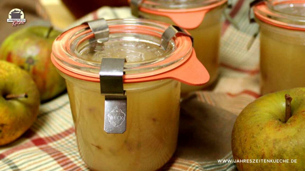Zwischen frischen braungrünen Äpfeln stehen Einmachgläser, die mit Gummiring und Klammern verschlossen sind.