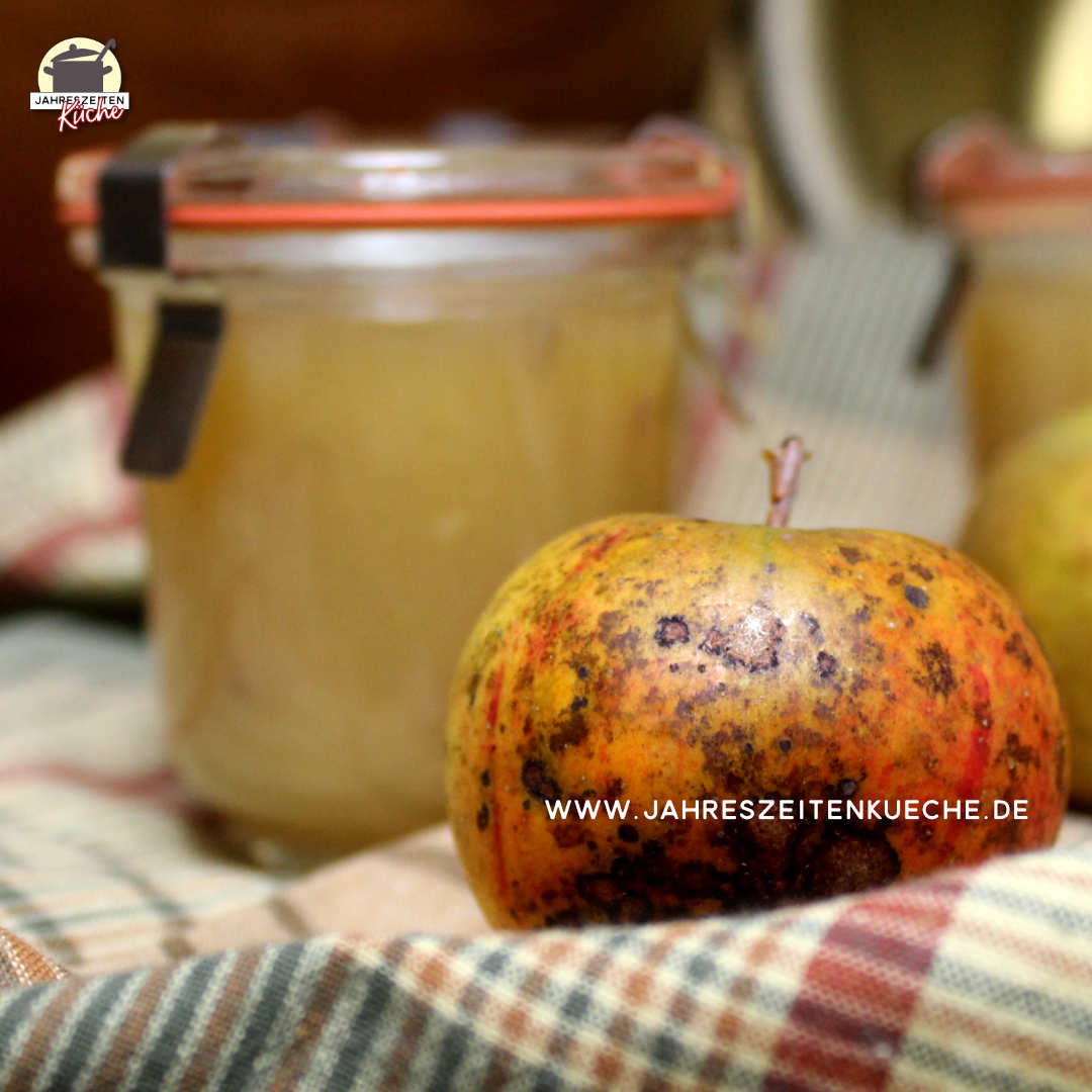 Vor einem Glas mit Apfel-Lavendel-Marmelade liegt ein rot-grüner Apfel.