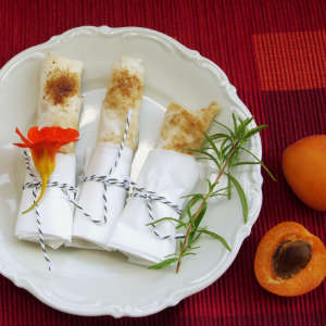 Auf einem Porzellanteller liegen drei süße Börek, die in Pergamentpapier eingewickelt sind.