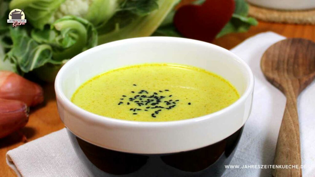 Ein Schüssel mit Blumenkohlsuppe. Daneben liegt ein Holzlöffel.