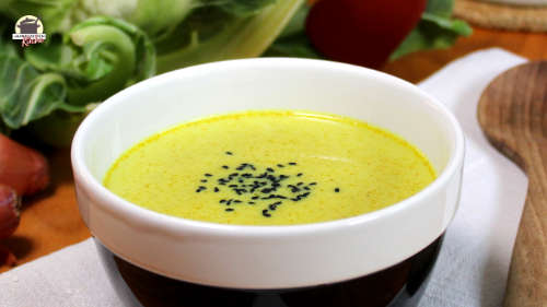 Ein Schüssel mit Blumenkohlsuppe. Daneben liegt ein Holzlöffel.