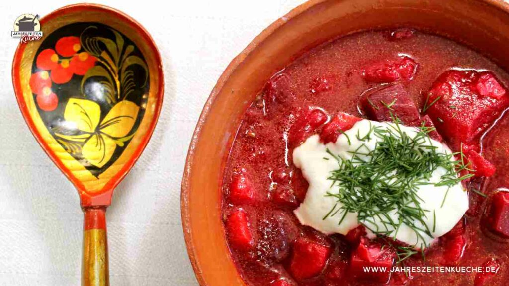 Ein mit Blumen bemalter Löffel liegt links neben einer Tonschüssel mit Borschtsch.