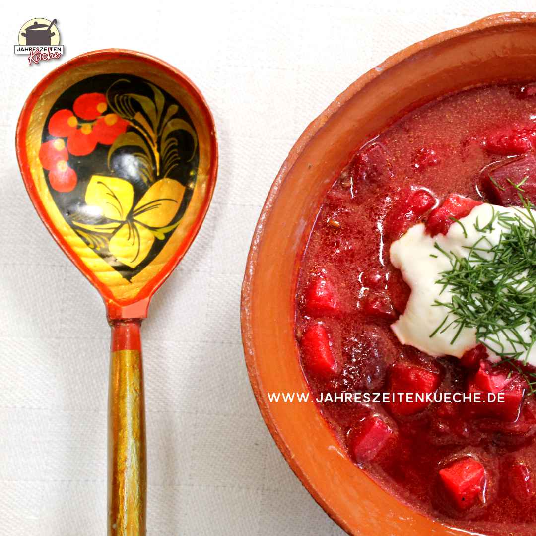 Ein mit Blumen bemalter Löffel liegt links neben einer Tonschüssel mit Borschtsch.