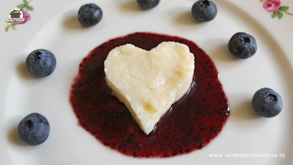 Buttermilchreis in Herzform liegt in einem Spiegel aus Heidelbeermark.