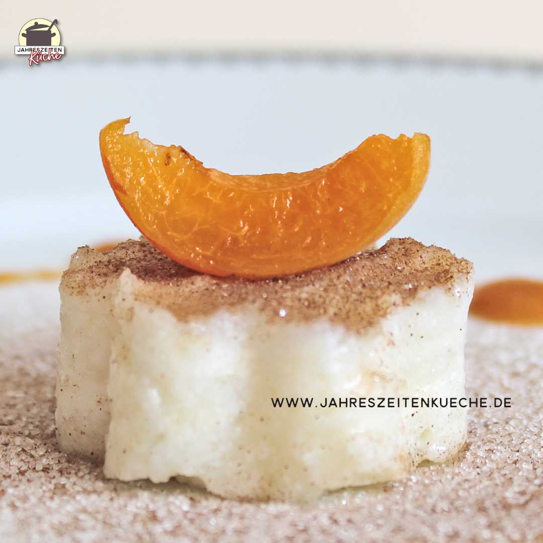 Eine Aprikosenspalte liegt auf einer Portion Buttermilchreis, die Zimt-Zucker bestreut ist.