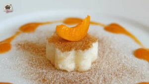 Buttermilchreis in Form einer kleinen Blume mit Zimt-Zucker bestreut. Darauf liegt eine Aprikosenspalte.