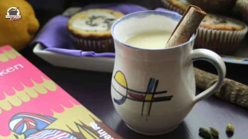 Chai mit Zimtstange in einer Tasse. Daneben liegt das Buch "Kuchen backen in Kigali"
