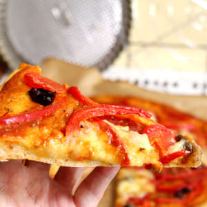 Ein Stück Dinkelpizza mit Paprika, Oliven und Mozzarella.