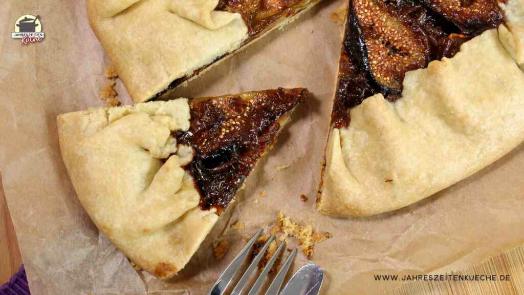 Ein Stück Feigen-Galette ist aus einer großen Galette herausgeschnitten. Beides liegt auf einem Holzbrett.