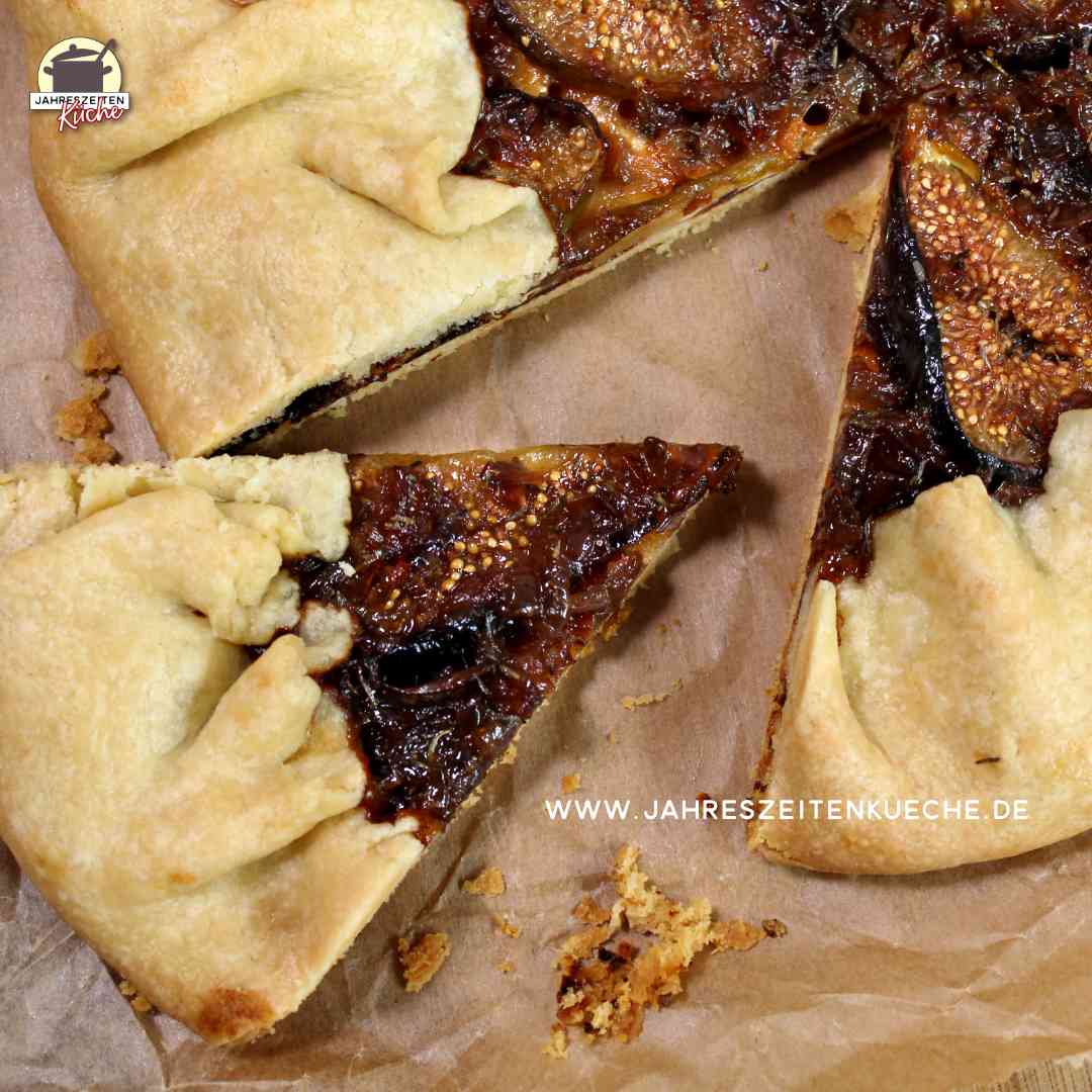 Eine Galette mit Feigen und Camembert liegt auf Backpapier. Ein Stück davon ist herausgeschnitten.