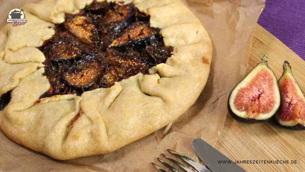 Auf einem Holzbrett liegt eine Feigen-Galette neben einer aufgeschnittenen Feige.