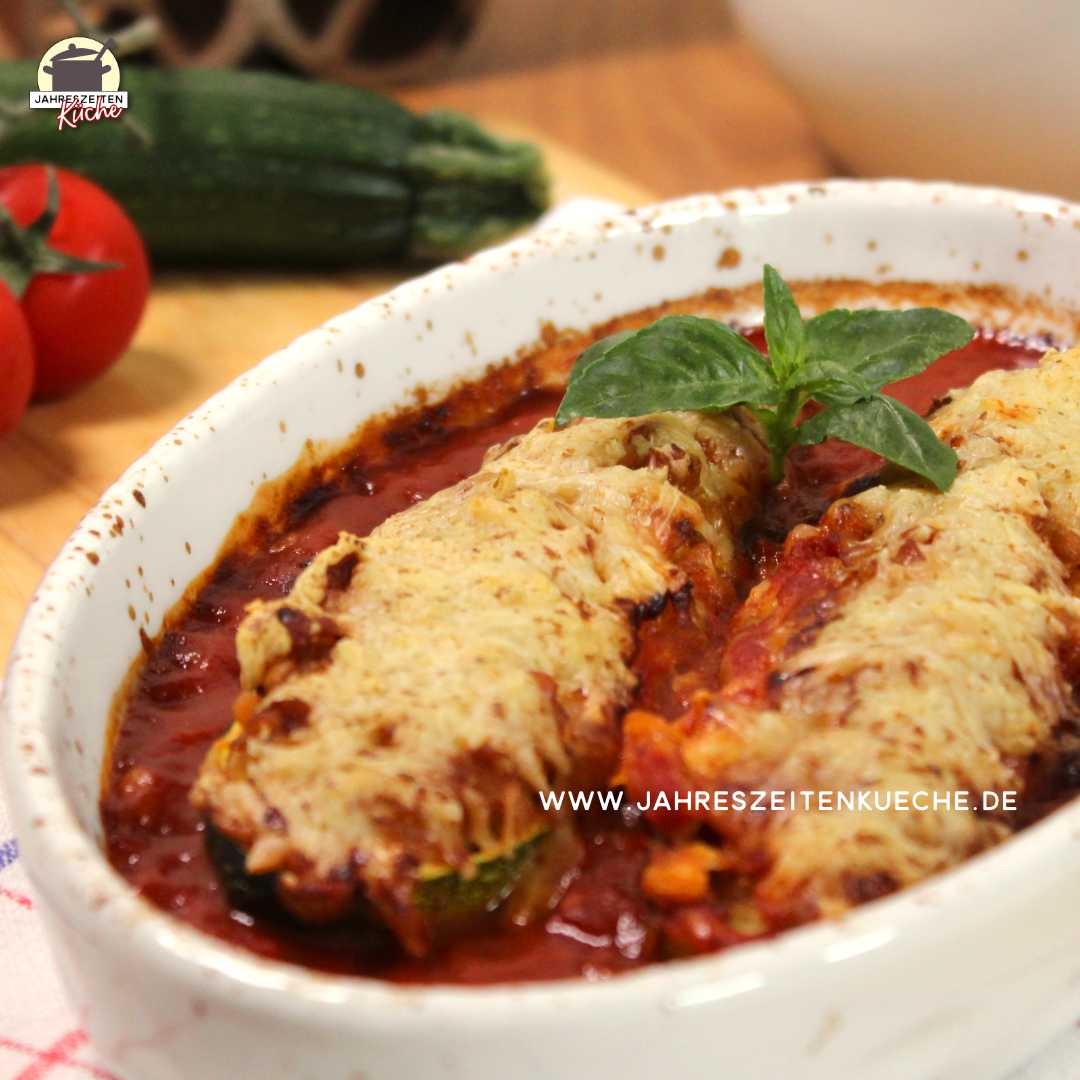 In einer ovalen Keramikform liegen zwei gefüllte Zucchinis, die mit Käse überbacken und mit Basilikumblättern garniert sind.