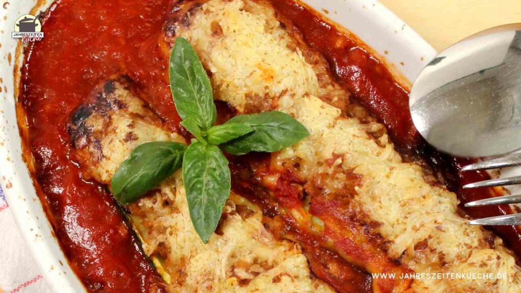 Bildausschnitt von einer Auflaufform mit zwei gefüllten Zucchinis. Darauf liegen Basilikumblätter