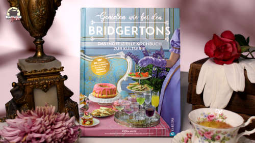 Das Kochbuch Genießen wie bei den Bridgertons ist eingerahmt von einem alten Kerzenleuchter und einem Stapel Bücher, auf denen weiße Handschuhe und eine rote Rose liegen.