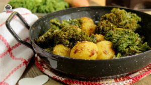 Eine emaillierte Pfanne mit Sesamkartoffeln und Grünkohl steht auf einem rot-weißen Untersetzer.