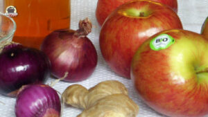 Auf einem weißen Tischtuch liegen die Zutaten für das Chutney Grundrezept: Essig, rote Zwiebeln, Äpfel und Ingwer