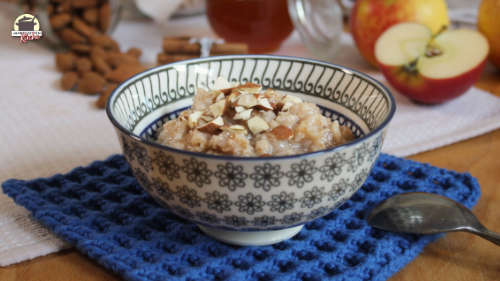 Ein Schälchen mit Habermus auf einem blauen Deckchen. Im Hintergrund liegen Äpfel, Honig und Mandeln.