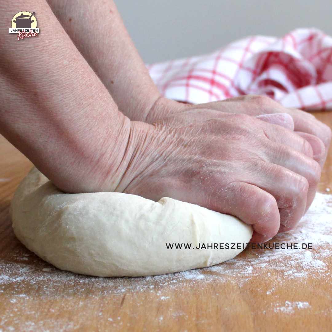 Zwei Hände kneten Teig auf einem Holztisch