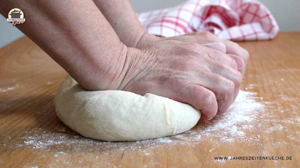 Auf einem Holztisch wird Hefeteig geknetet