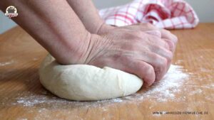 Auf einem Holztisch wird Hefeteig geknetet