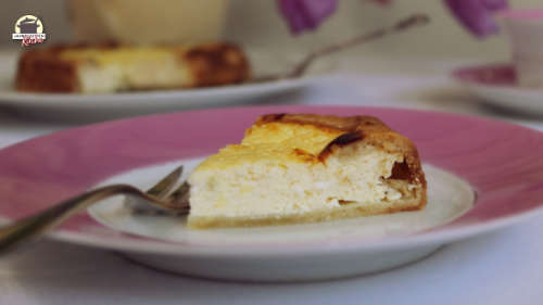 Ein Stück Hüttenkäsekuchen auf einem Teller mit rosafarbenem Rand.