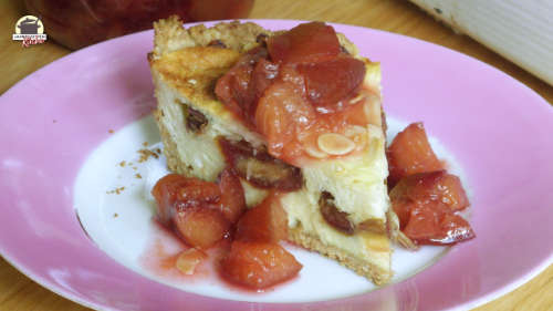 Auf einem Porzellanteller mit rosafarbenen Rand ist ein Stück Käsekuchen mit Datteln und Zwetschgenkompott.