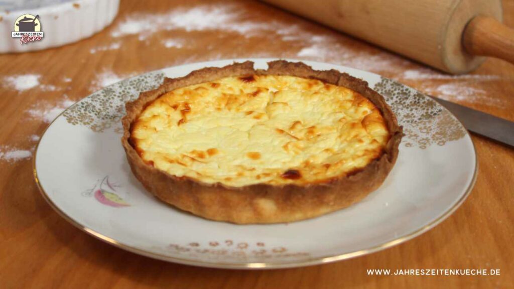 Auf einem mit Mehl bestäubten Tisch steht ein Teller mit einem kleinen Hüttenkäsekuchen