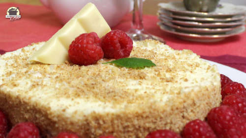 Mitten auf einem Käsekuchen ohne backen liegen zwei Himbeeren und ein großes Stück weiße Schokolade.
