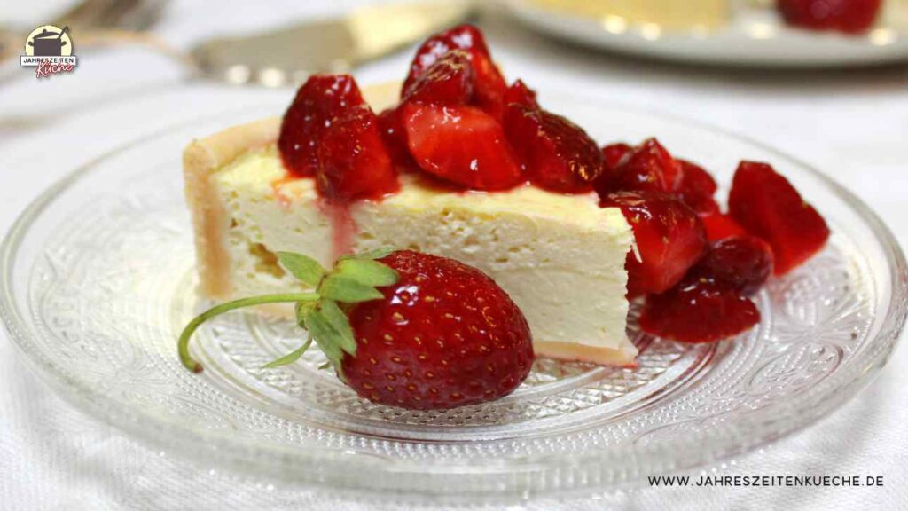 Ein Stück Käsekuchen mit versoffenen Erdbeeren liegt auf einem Glasteller.