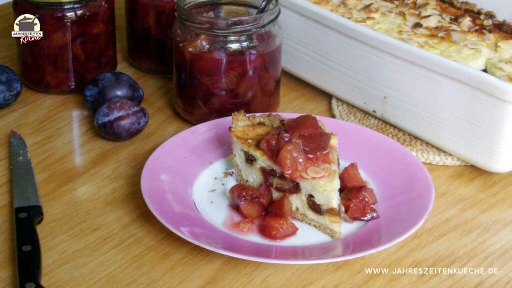 Ein Stück Käsekuchen auf einem Teller. Im Hintergrund mehrere Gläser Zwetschgenkompott.
