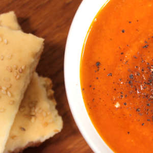 Eine weiße Suppenschale mit Karotten-Tomaten-Suppe. Links daneben liegt Lavashbrot.