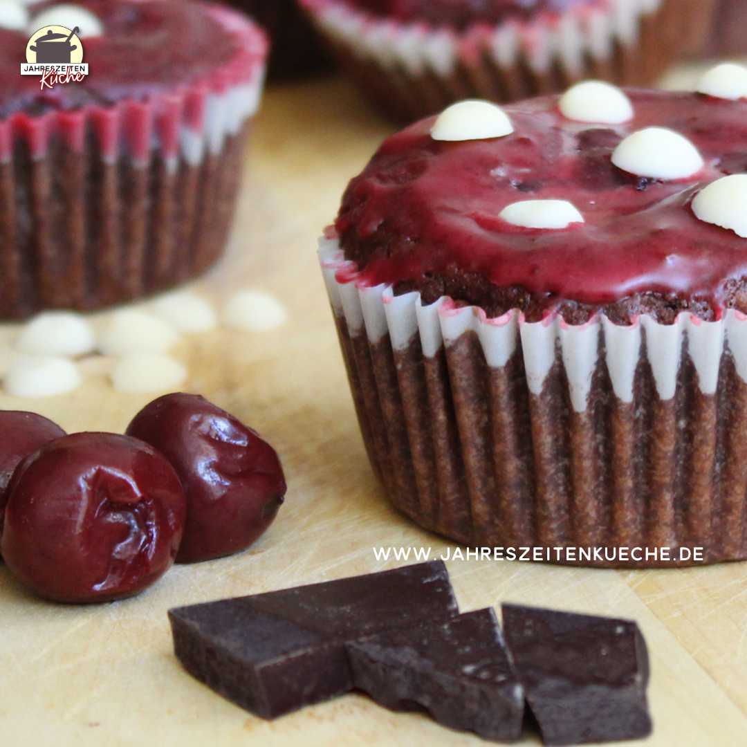 Vor einem Kirsch-Schoko-Muffin, der wie Fliegenpilz aussieht, liegen Schokoladenstücke und Kirschern.