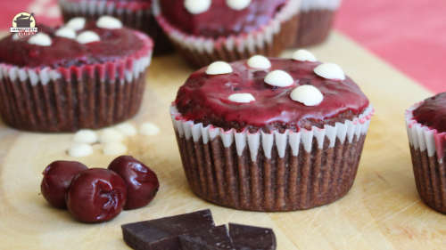 Auf einem Holzbrrett stehen Schoko-Kirsch-Muffins, die wie Fliegenpilze aussehen