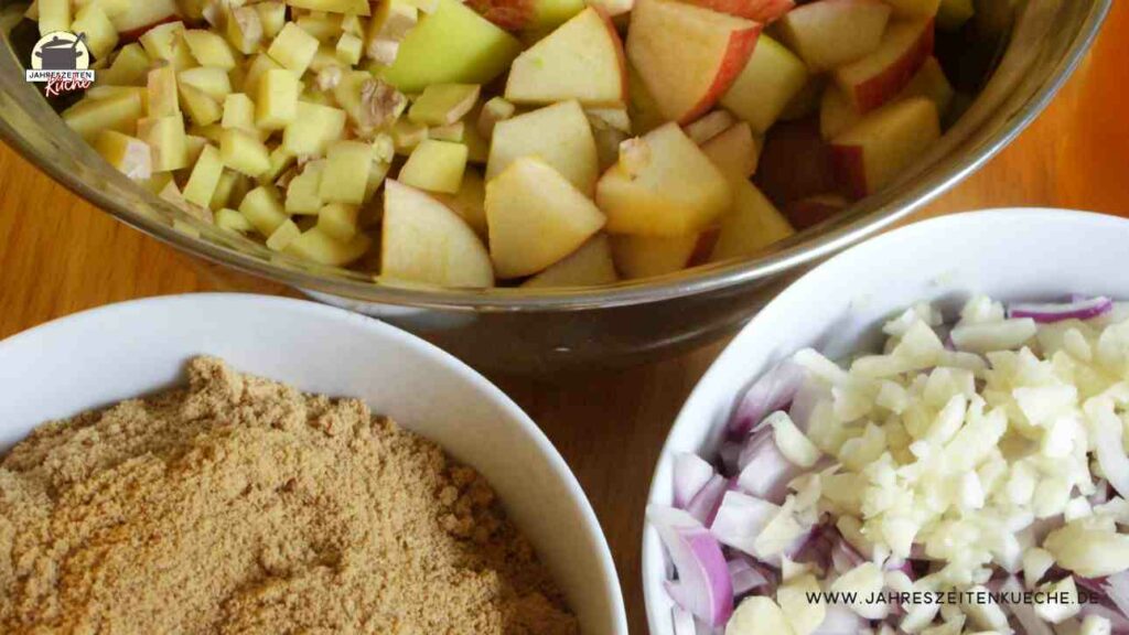 Klein geschnittene Äpfel, Ingwer, Zwiebeln, Knoblauch und und brauner Zucker stehen in Schüsseln bereit