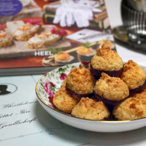 Rechts neben einer Einladungskarte von Lady Whistledown steht ein Teller mit Kokosmakronen