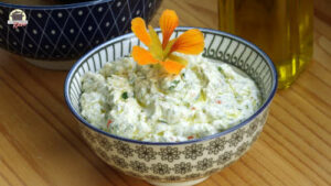 Eine Portion selbstgemachter Kräuterquark mit frischen Kräutern steht auf einem Holztisch