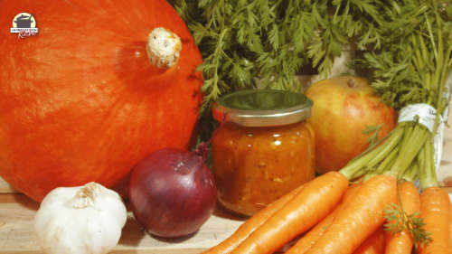 Ein Glas Kürbis-Chutney steht zwischen Hokkaido-Kürbis, Karotten, Zwiebeln und Apfel
