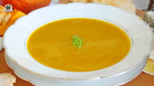 Ein weißer Teller mit Kürbis-Fenchelsuppe. Im Hintergrund liegt ein Hokkaidokürbis.