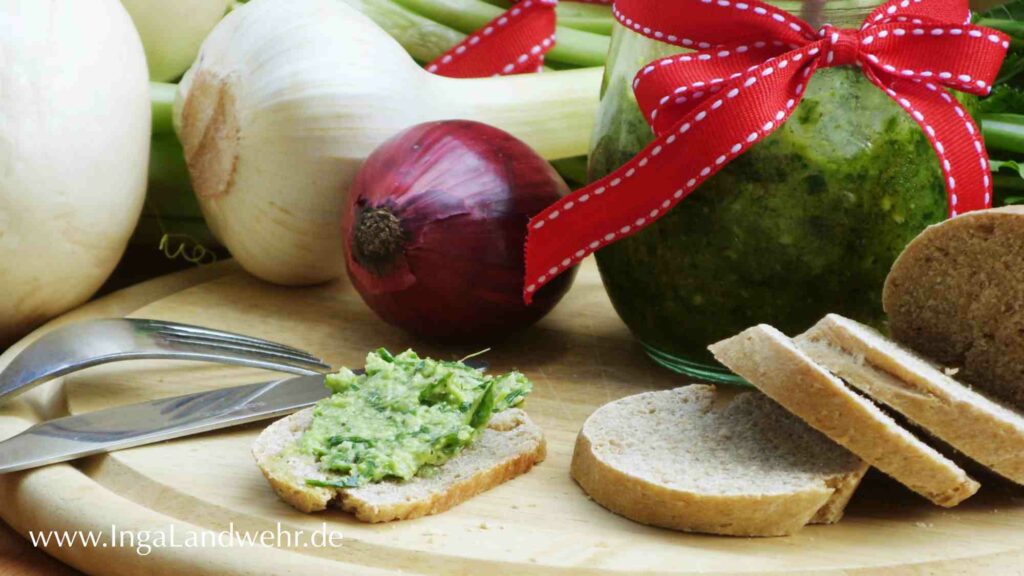 Eine Scheibe Khorosan-Dinkel-Baguette mit Mairübchen-Pesto bestrichen liegt auf einem Holzbrett