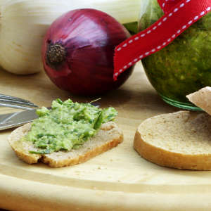 Eine rote Zwiebel und eine Scheibe Khorosan-Dinkel-Baguette mit Mairübchen-Pesto liegen auf einem Holzbrett