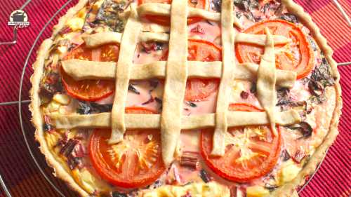 Mangold-Quiche mit Tomatenscheiben und einem Gitter aus Teigstreifen.