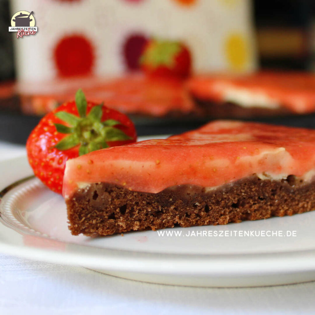 Die Spitze von einem Stück Küchen. Im Hintergrund liegt eine Erdbeere.