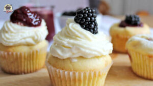 Ein Muffin mit Vanillepudding-Frosting. Darauf liegt eine Brombeere.