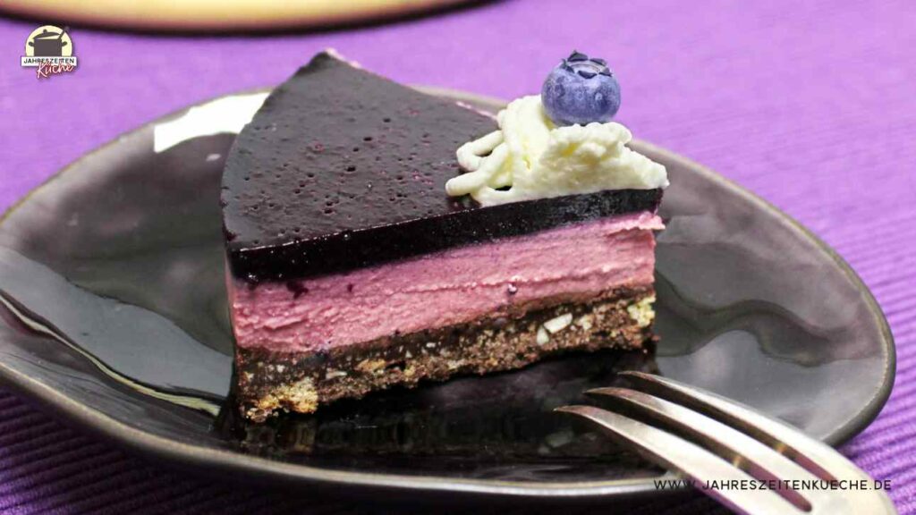 Auf einem braunen Keramikteller liegt ein Stück Käsekuchen mit Heidelbeeren.