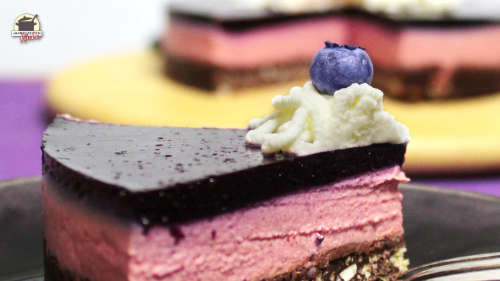 Ein Stück No-Bake-Käsekuchen liegt auf einem Teller. Im Hintergrund ist der aufgeschnittene Kuchen zu sehen.