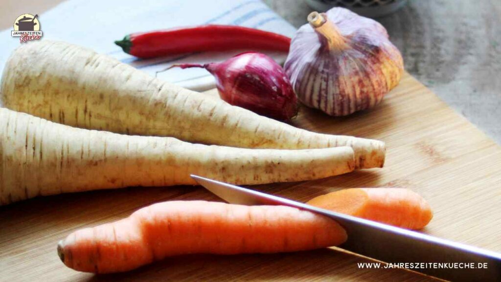 Pastinaken, Karotten, Zwiebeln und Knoblauch auf einem Holzbrett