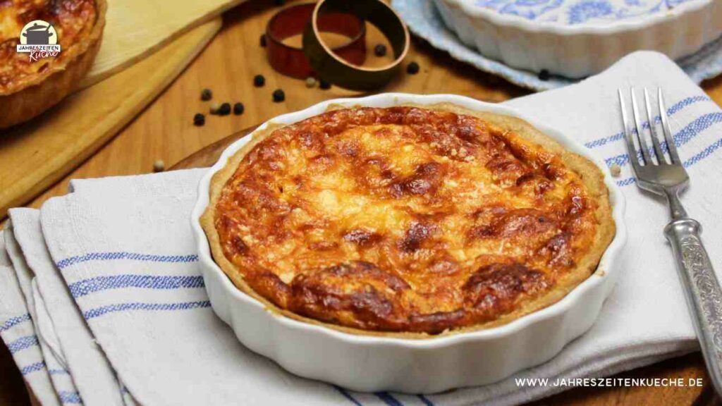 Pastinaken-Quiche in einer weißen Single-Quiche-Form steht auf einem grau-blauem Untersetzer.Pastinaken-Quiche in einer weißen Single-Quiche-Form steht auf einem grau-blauen Untersetzer.